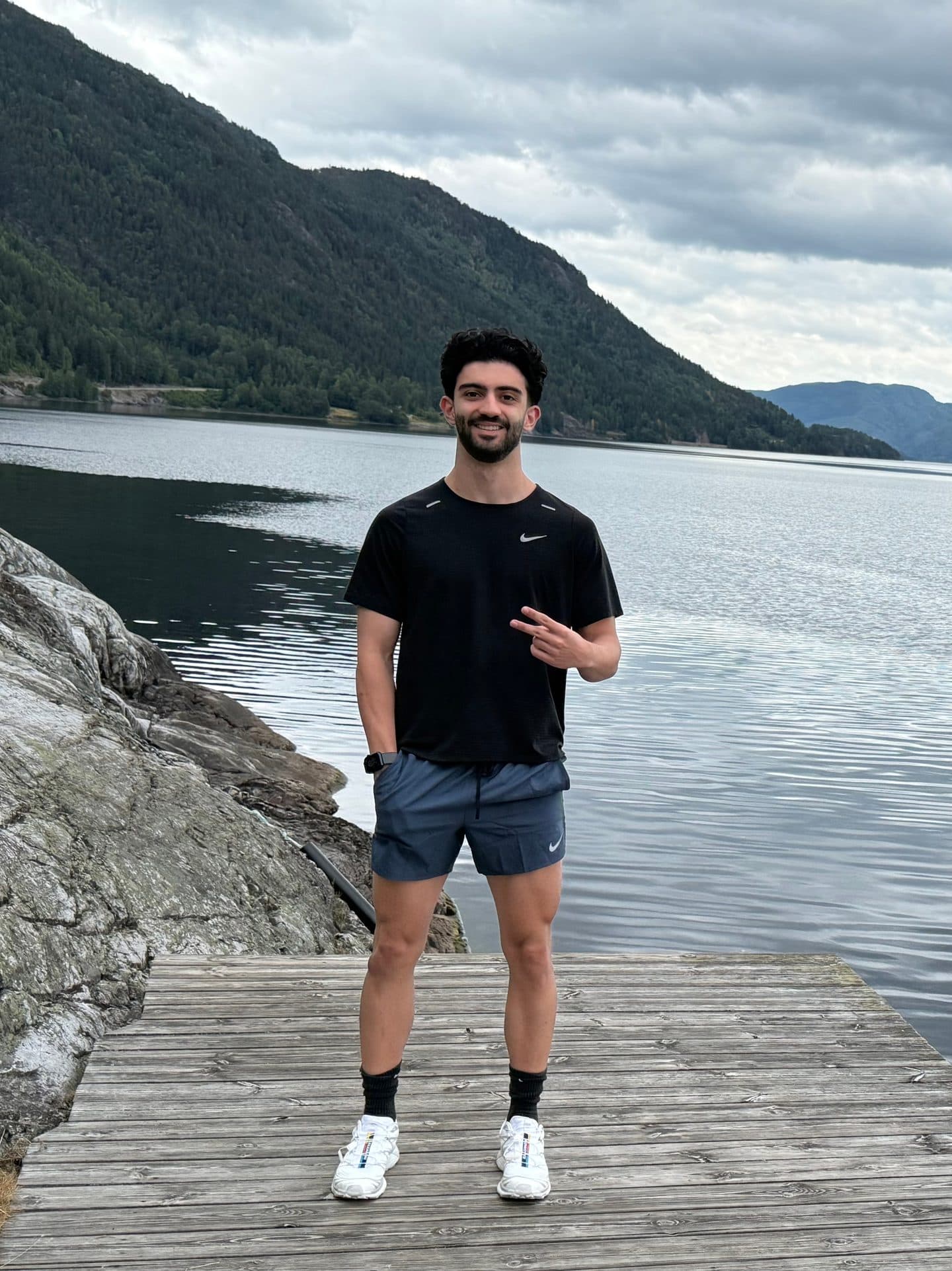 Mahyar standing on a wooden dock by the water in Norway, with mountains behind him