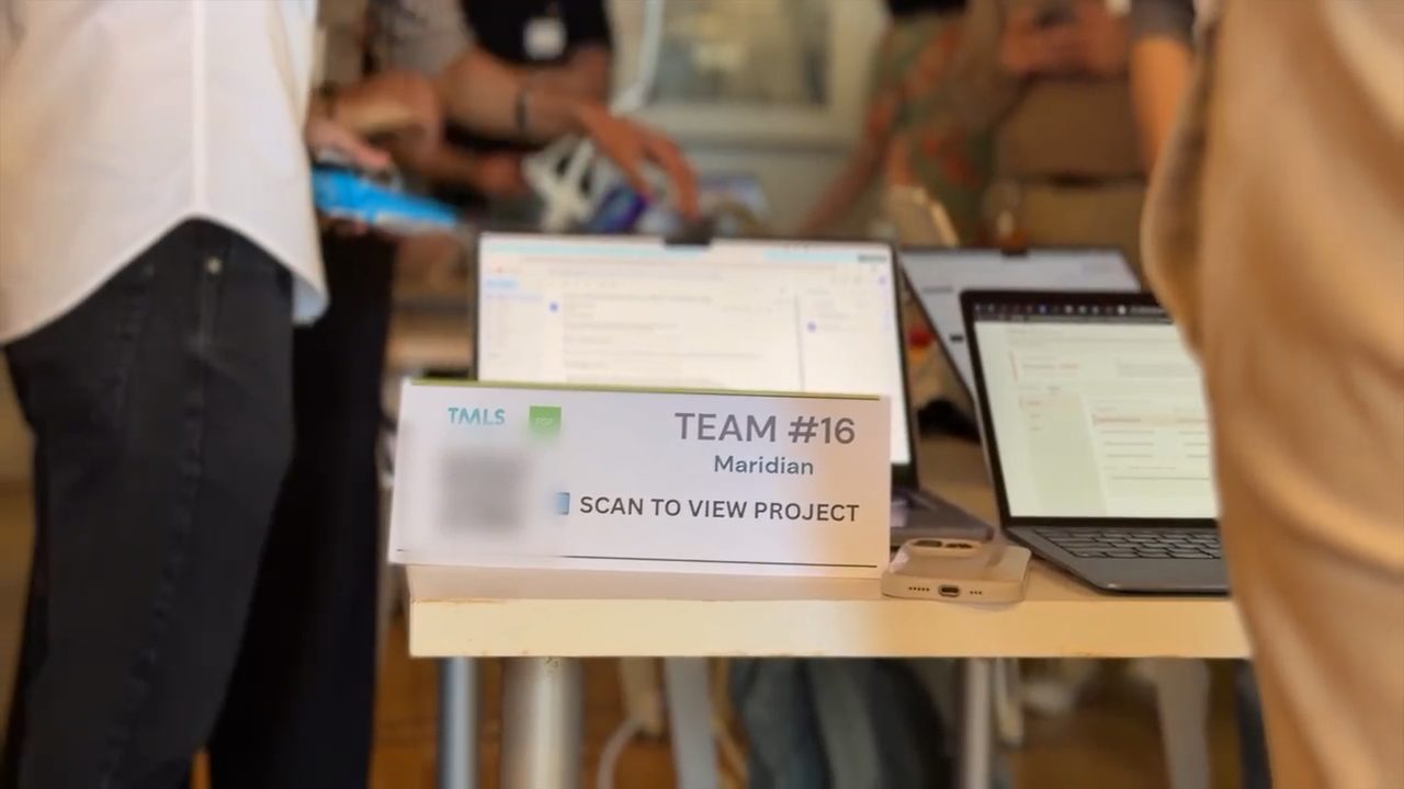 A handheld shot past people standing at the team’s table, coming to rest on its sign: “TMLS · Team #16 · Maridian · Scan to view project”, the QR code blurred, in front of two open laptops.